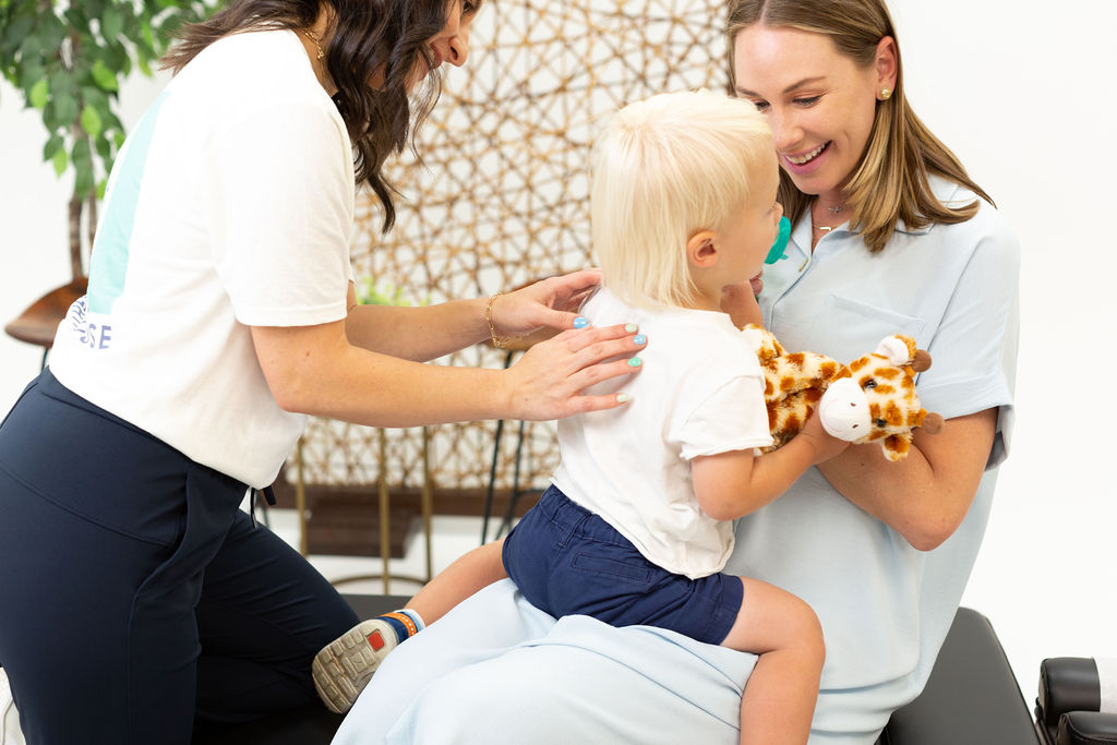 Dr. Jessica assessing a kid while kid's mom holds him- Lighthouse Chiropractic and Wellness